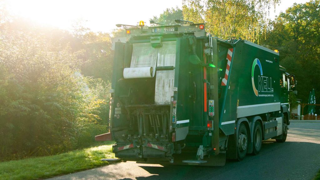 KELL-Müllfahrzeug aus der Heckansicht im Einsatz auf einer Straße bei tiefstehender Sonne – Symbolbild für Entsorgung und Abfallvermeidung.